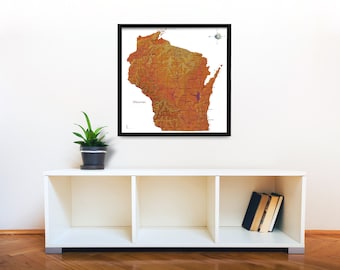 Puede incluir: Un mapa enmarcado de Wisconsin con un diseño de relieve topográfico detallado. El mapa está impreso en tonos naranja y marrón, con un marco negro. El mapa está colgado en una pared blanca sobre un estante blanco con una planta en maceta y libros.
