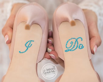 May include: A pair of light pink high-heeled shoes with blue rhinestone embellishments spelling out "I do" on the soles.