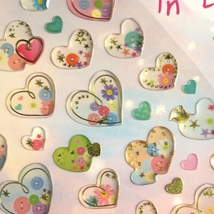 May include: A sheet of colorful heart-shaped stickers with a gold outline. The hearts are decorated with buttons, flowers, and stars. The text "Love in the sky" is printed on the sheet. Love is something like the clouds that were in the sky before the sun came out.