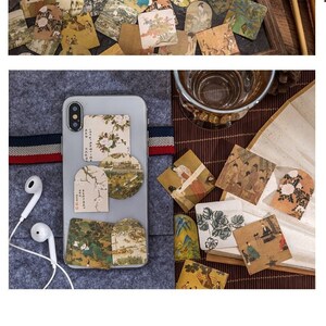 May include: 45 paper stickers with a vintage Japanese aesthetic. The stickers feature illustrations of landscapes, people, and buildings. The stickers are arranged on a variety of surfaces, including a notebook, a phone case, and a wooden tray.