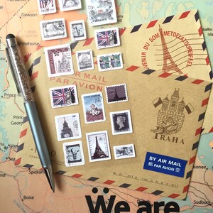 May include: A brown paper envelope with a red and blue striped border. The envelope has a stamp with a drawing of the Eiffel Tower and the text "VENIR DU SOM METDELATOUREIF TRAHA BY AIR MAIL 航 PAR AVION 空". The envelope is decorated with various postage stamps featuring landmarks from around the world. The text "We are the world" is printed on a map below the envelope.
