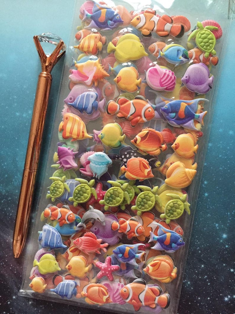 Puede incluir: Una bolsa de pl&aacute;stico transparente llena de pegatinas de espuma 3D de colores de criaturas marinas, incluyendo peces, tortugas y estrellas de mar. Las pegatinas est&aacute;n dispuestas en filas y columnas, y hay una variedad de colores y dise&ntilde;os. Un bol&iacute;grafo dorado con una parte superior en forma de diamante est&aacute; al lado de la bolsa.