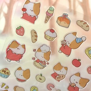 K&ouml;nnte beinhalten: Eine Blatt mit transparenten Aufklebern mit niedlichen Comic-Katzen in roten Kleidern, die verschiedene Lebensmittel wie Brot, Kuchen und Eis halten. Die Aufkleber enthalten auch Erdbeeren, &Auml;pfel und andere Lebensmittelmotive.