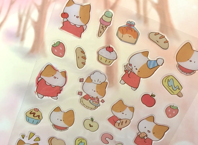 K&ouml;nnte beinhalten: Eine Blatt mit transparenten Aufklebern mit niedlichen Comic-Katzen in roten Kleidern, die verschiedene Lebensmittel wie Brot, Kuchen und Eis halten. Die Aufkleber enthalten auch Erdbeeren, &Auml;pfel und andere Lebensmittelmotive.