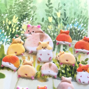 May include: A collection of 12 colorful hamster stickers with different poses. The stickers are made of a soft, puffy material and have a glossy finish. The hamsters are all wearing different expressions and have different colored fur.