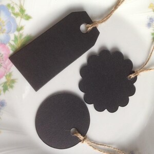 May include: Three black paper gift tags with twine string. The tags are different shapes: a circle, a scalloped circle, and a rectangle.