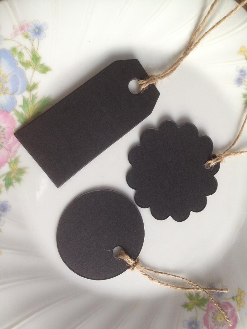 May include: Three black paper gift tags with twine string. The tags are different shapes: a circle, a scalloped circle, and a rectangle.