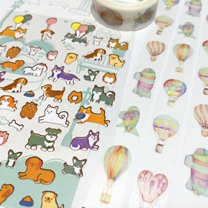 May include: A sheet of colorful dog stickers with a variety of breeds and poses. The stickers are on a white background. There are also three rolls of washi tape with watercolor hot air balloons on a white background.