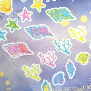 May include: A sheet of colorful stickers featuring seashells, starfish, and coral. The stickers are on a clear background with a purple hue.