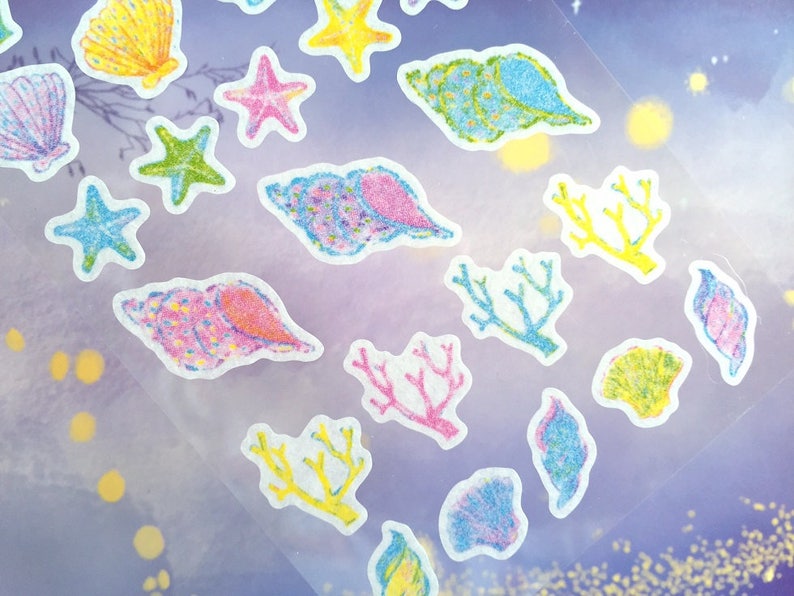 May include: A sheet of colorful stickers featuring seashells, starfish, and coral. The stickers are on a clear background with a purple hue.