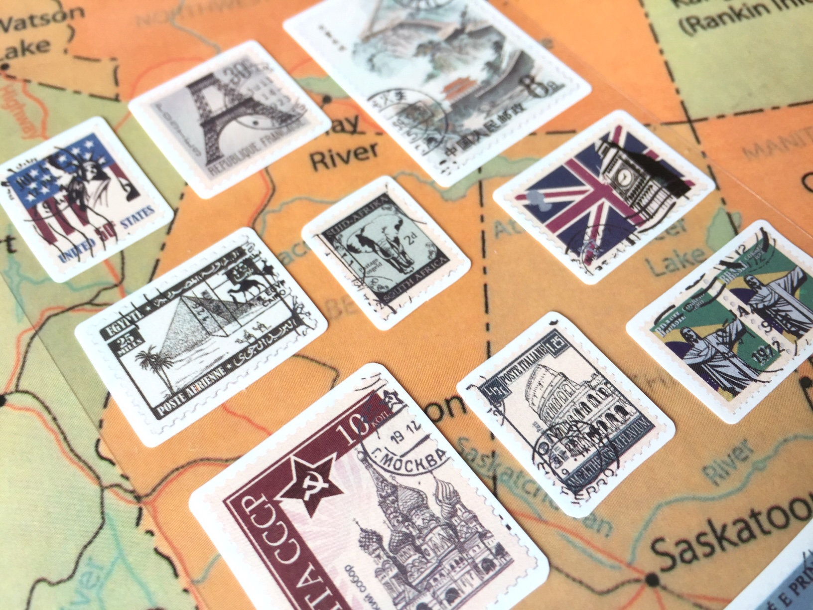 May include: A collection of vintage postage stamps featuring iconic landmarks from around the world, including the Eiffel Tower, Big Ben, the Statue of Liberty, and the Kremlin. The stamps are arranged on a map of North America.