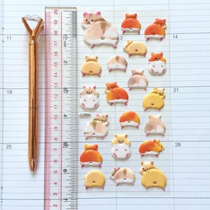 May include: A sheet of colorful hamster stickers with a ruler and a gold pen. The stickers feature hamsters in various poses, including sitting, standing, and running. The stickers are perfect for adding a touch of whimsy to planners, journals, and other paper goods.