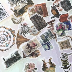 Puede incluir: Una colección de pegatinas de estilo vintage con varios diseños, que incluyen un tren, un reloj, una tetera, un conejo y una botella. Las pegatinas están impresas en papel transparente y claro y tienen un aspecto desgastado y antiguo.