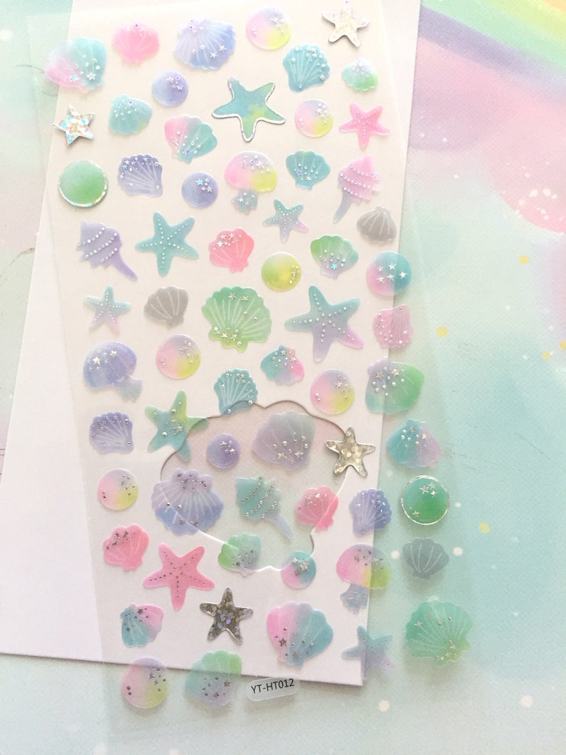 May include: A sheet of iridescent stickers featuring seashells and starfish in various pastel colors. The stickers are on a clear background and have a glittery finish. The sheet is labeled "YT-HT012".