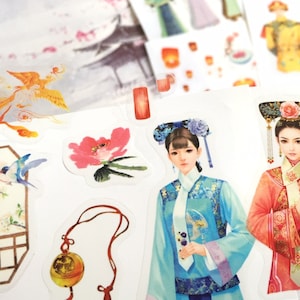 Peut inclure: Une feuille d'autocollants illustrant des femmes en costumes traditionnels chinois, un phénix, une fleur, un oiseau sur une branche et un pendentif décoratif. Les autocollants sont sur fond blanc.