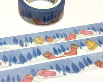 May include: A roll of blue washi tape with a wintery design featuring trees, mittens, boots, and yarn balls. The tape has a white background and is decorated with a light blue pattern.