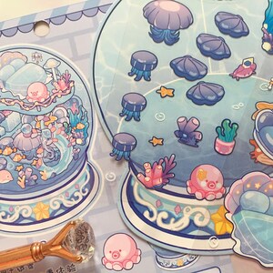 May include: A sheet of colorful stickers featuring an underwater theme. The stickers include jellyfish, octopuses, seashells, coral, and other sea creatures in shades of blue, pink, and purple. The stickers are arranged in a whimsical, cartoon style.