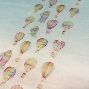 May include: A sheet of colorful washi tape with a repeating pattern of hot air balloons. The balloons are drawn in a watercolor style with various colors and patterns.
