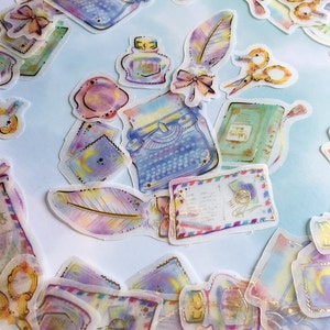 Könnte beinhalten: Ein Bogen durchsichtiger, bunter Aufkleber mit Vintage-inspirierten Illustrationen einer Schreibmaschine, Tintenflaschen, Federn, Briefumschlägen und Scheren. Die Aufkleber haben einen Aquarell-Effekt und goldene Akzente.