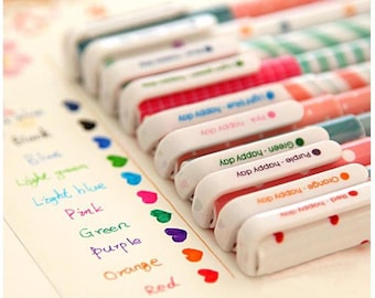 May include: A set of ten colorful gel pens with white barrels and colorful polka dot designs. Each pen has a different color ink and a label with the color name and the phrase "Happy Day".