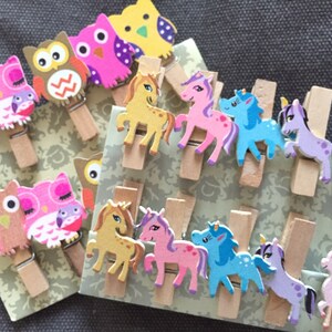 May include: A set of wooden clothes pegs with colourful animal designs. The set includes owls and unicorns in pink, purple, blue, brown and yellow.