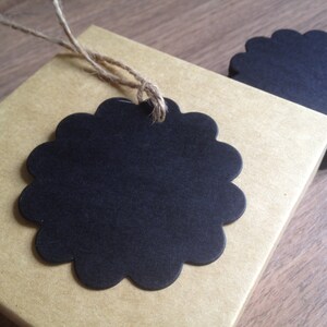 May include: A stack of black scalloped circle gift tags with twine attached. The tags are on a brown paper surface.