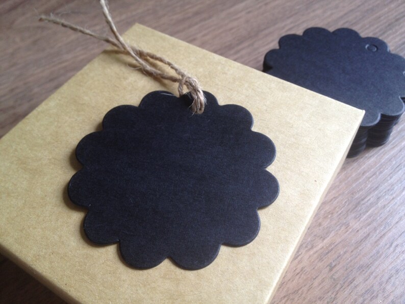 May include: A stack of black scalloped circle gift tags with twine attached. The tags are on a brown paper surface.