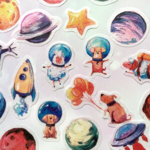 Puede incluir: Un conjunto de pegatinas coloridas con ilustraciones de tem&aacute;tica espacial, que incluyen planetas, estrellas, cohetes y animales. Las pegatinas son perfectas para a&ntilde;adir un toque caprichoso a diarios, port&aacute;tiles u otras superficies.