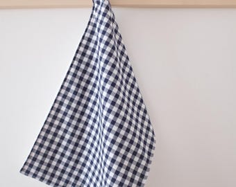 Op de afbeelding: Een blauwe en witte gingham keukendoek hangt aan een houten rek. De doek heeft een klein wit label met het woord "SEASON" erop.