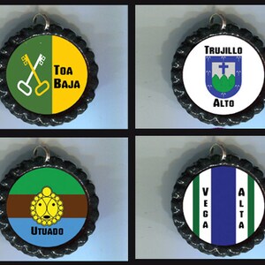 May include: Four bottle cap charms with different designs. The first charm is green and yellow with a pair of crossed keys and the text "TOA BAJA". The second charm is white with a green and white crest and the text "TRUJILLO ALTO". The third charm is green, brown, and blue with a yellow sun design and the text "UTUADO". The fourth charm is white with green and blue stripes and the text "VEGA ALTA".