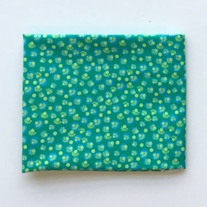 Könnte beinhalten: Grüner Stoff mit einem sich wiederholenden Muster aus kleinen, hellgrünen und blauen Kreisen. Die Kreise haben einen weißen Umriss und eine hellgrüne Mitte.