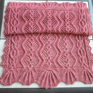 May include: A pink knitted shawl with a lacy pattern. The shawl has a scalloped edge and is folded in half.