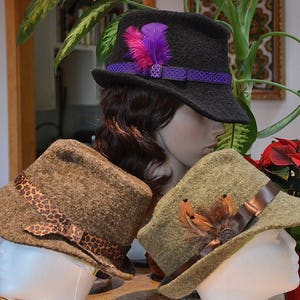 May include: Three felt hats in different colors and styles. The first hat is black with a purple ribbon and a purple feather. The second hat is brown with a leopard print band. The third hat is green with a brown band and a brown feather.