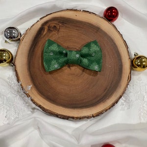 May include: A green bow tie with a snowflake pattern on a wooden surface.