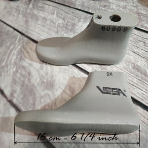 Puede incluir: Dos hormas de zapatos de plástico gris, una con el número 60909 impreso en ella y la otra con el número 24 y la palabra "VEGA" impresa en ella. La horma más grande mide 16 cm o 6 1/4 pulgadas de largo.