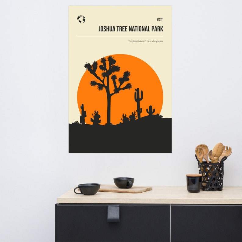 May include: A minimalist poster with a black silhouette of a Joshua Tree and other desert plants against an orange sunset. The text "VISIT JOSHUA TREE NATIONAL PARK" is at the top of the poster, and the text "The desert doesn't care who you are" is below the image.