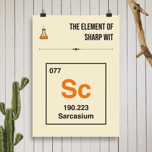 Op de afbeelding: Een poster met de tekst "THE ELEMENT OF SHARP WIT" en een afbeelding van een fles. Daaronder staat in een vak in de stijl van het periodiek systeem "077 Sc 190.223 Sarcasium" in oranje en zwart. De poster is vastgezet op een witte houten achtergrond.