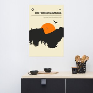 Op de afbeelding: Een poster in retro-stijl met een zwart silhouet van een bergketen en een ondergaande zon. De tekst luidt "BEZOEK HET ROCKY MOUNTAIN NATIONAL PARK. De vrede van de natuur zal in je stromen als zonlicht in de bomen."