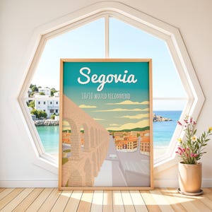 Op de afbeelding: Een ingelijste reisposter met de stad Segovia, Spanje. De poster toont een gestileerde illustratie van het Romeinse aquaduct, met het woord "Segovia" in witte letters boven de zin "10/10 would recommend". De poster staat tegen een turquoise en blauwe lucht.