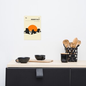 Peut inclure: Une affiche minimaliste avec un fond beige repr&eacute;sentant une silhouette noire de Monument Valley avec un grand soleil orange en arri&egrave;re-plan. Le texte "Monument Valley" est imprim&eacute; en noir en haut de l'affiche.