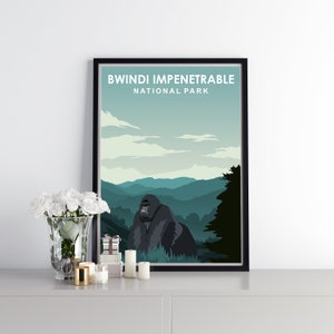 Op de afbeelding: Een zwart ingelijste poster met een groene en blauwe landschapsscène van bergen en een gorilla op de voorgrond. De tekst "BWINDI IMPENETRABLE NATIONAL PARK" staat bovenaan de poster.