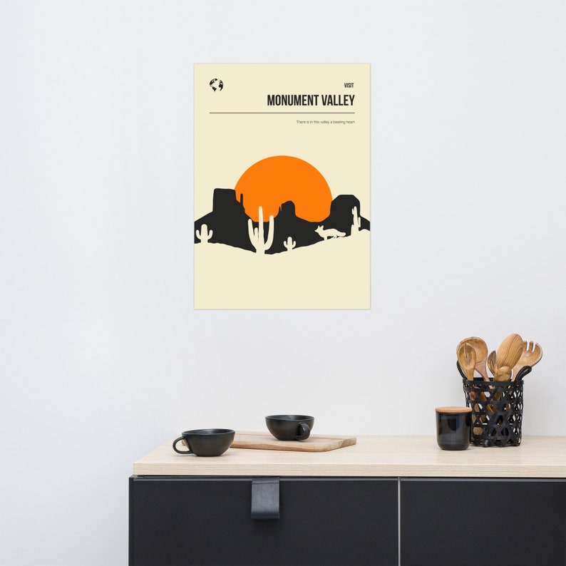 Peut inclure: Une affiche minimaliste avec une silhouette noire d'un paysage d&eacute;sertique avec un grand soleil orange, avec le texte "Monument Valley" et "There is in this valley a healing heart".