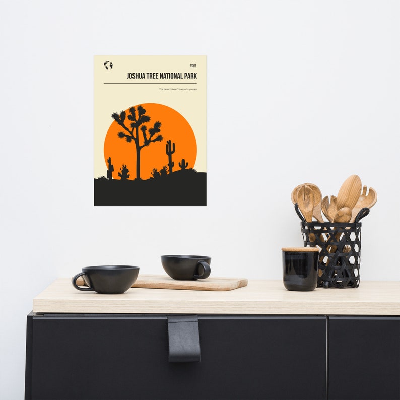 May include: A minimalist poster with a black silhouette of a Joshua Tree and cacti against an orange sunset. The text "VISIT JOSHUA TREE NATIONAL PARK" is at the top of the poster. The text "The desert doesn't care why you are here" is below the image.