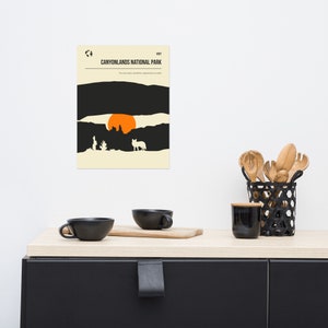 Może przedstawiać: Minimalistyczny plakat w czarno-pomarańczowej kolorystyce przedstawiający zach&oacute;d słońca nad pustynnym krajobrazem. Tekst "VISIT CANYONLANDS NATIONAL PARK" znajduje się u g&oacute;ry plakatu. Tekst "The most weird, wonderful, magical place on earth" znajduje się pod nazwą parku.