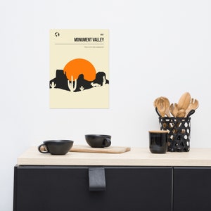 Peut inclure: Une affiche minimaliste avec un fond beige repr&eacute;sentant une silhouette noire d'un paysage d&eacute;sertique avec un grand soleil orange, des cactus et un coyote. Le texte "VISIT MONUMENT VALLEY" est en noir en haut de l'affiche.