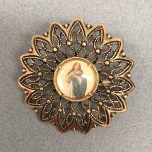 May include: A gold-toned metal brooch with a filigree design. The center of the brooch features a round image of a woman in a blue dress holding a baby.