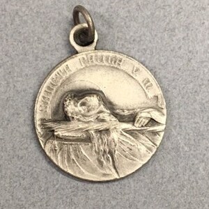 May include: Silver pendant with a depiction of a dove carrying an olive branch. The pendant has the inscription "Pax in Terris" around the edge.