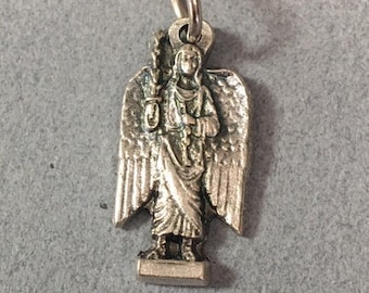 May include: Silver charm featuring a detailed depiction of an angel with wings outstretched, holding a staff. The angel is wearing a long robe and has a halo.