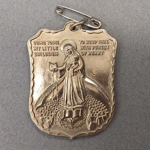 May include: Silver-toned metal religious charm with a depiction of the Virgin Mary holding a child. The charm is shaped like a shield and has the text "Come to me my little children" and "To keep thee with purest of heart" on it.