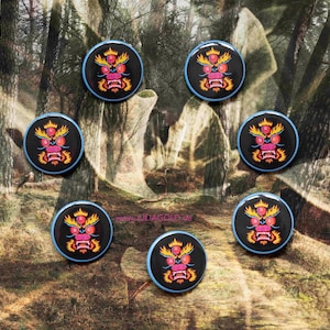 Op de afbeelding: Zeven ronde knoppen met een blauwe rand, een zwarte achtergrond en een rood en geel drakengezichtontwerp.